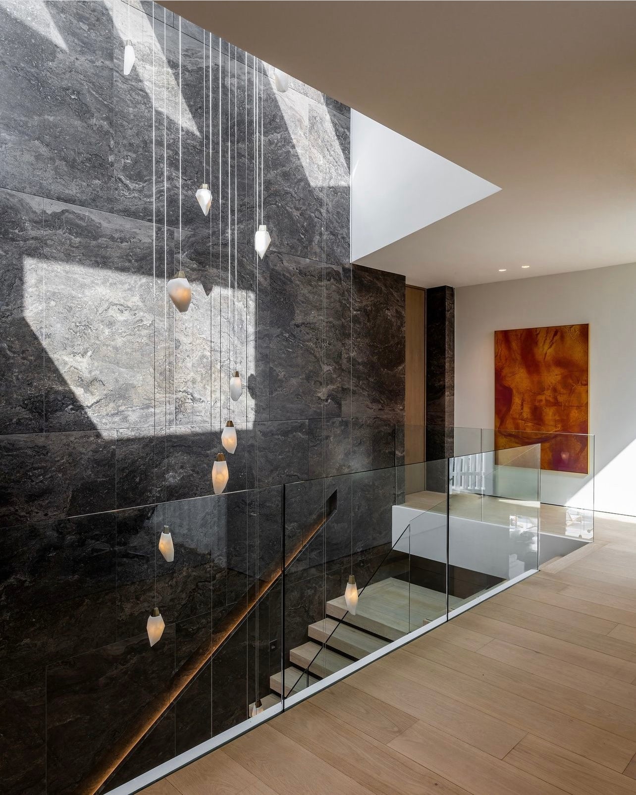 These Crystal shaped alabaster lights with bronze tops grouping are elegantly hung aginst this stone staircase wall. Available at Fathom Stone Art.