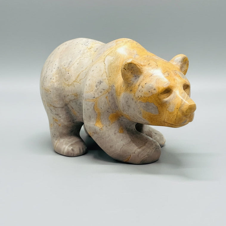 Small stone sculpture of a bear on a black stand with a blurred indoor background