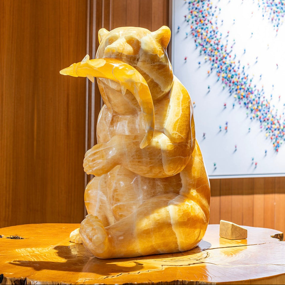 Decorative stone sculpture of a bear on a wooden surface with a colorful abstract painting in the background.