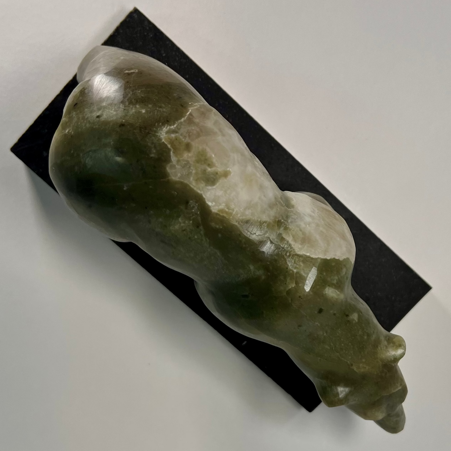 A polished carved stone sculpture of a bear walking on a rectangular black display plaque, photographed against a plain light background.