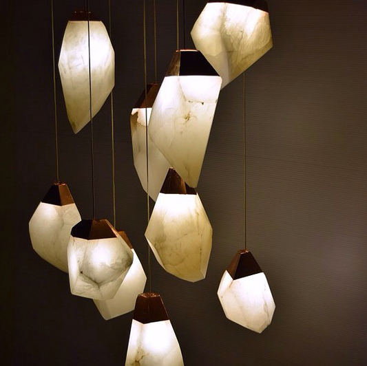 These elegant alabaster pendant lights showcase the natural beauty of hand-carved stone, with each piece offering its unique patterns and veining. Crafted from translucent white alabaster, these pendants emit a warm, diffused glow that brings a serene ambiance to any space. The photos highlight how these pendants catch the light, creating a soft gold hue when paired with warm bulbs, or choose a cooler temperature bulb for a brighter whiter glow.

Each pendant is accented with a choice of brass or bronze