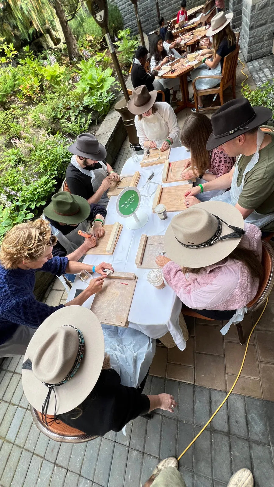A group in sun hats carving soapstone together at a long outdoor table